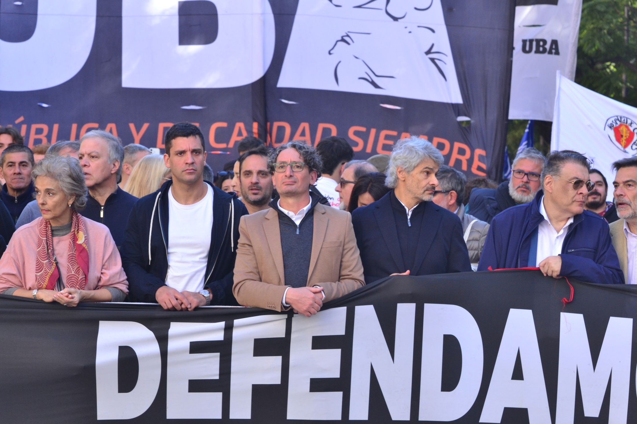 Emiliano Cagnacci junto a otras personas sostiene una bandera en una marcha de la UBA.